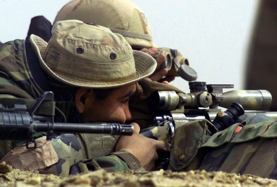 US Marine Corps (USMC) assigned as a Sniper with 1st Battalion, 4th Marine Regiment, Regimental Combat Team 1 (RCT-1), sights through the telescope mounted atop his 7.62mm M40A1 sniper rifle. US Navy (USN) Hospitalman (HN) Clint Sprabary acts as his spotter, at Al Shur, Iraq, during Operation IRAQI FREEDOM. Photo: Public Domain